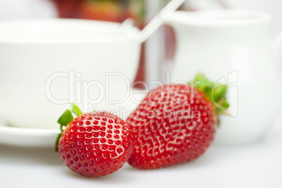 white cup and milk jug with strawberries isolated on white