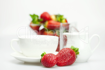 white cup and milk jug with strawberries isolated on white