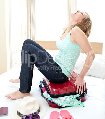 Laughing woman trying to close her suitcase