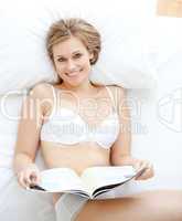 Happy woman reading a magazine lying on a bed