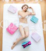 Smiling woman lying on a bed surrounded with shopping bags