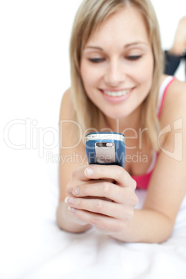 Young woman sending a text lying on a bed