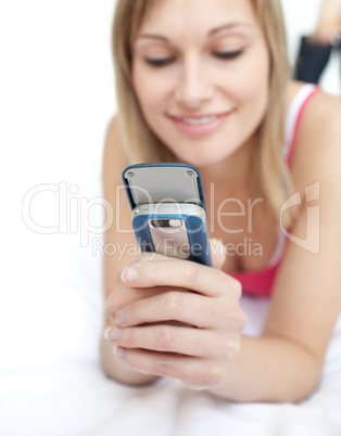 Blond woman sending a text lying on a bed