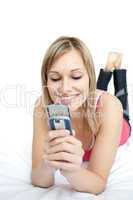 Bright woman sending a text lying on a bed