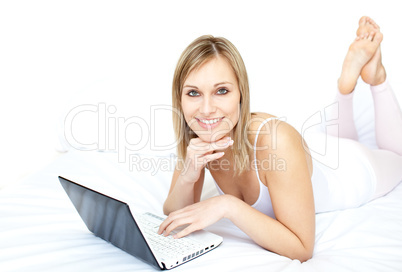 Cheerful woman using a laptop lying on her bed