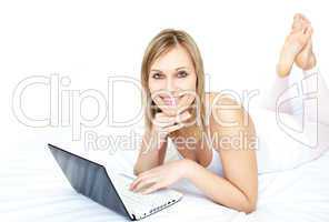 Cheerful woman using a laptop lying on her bed