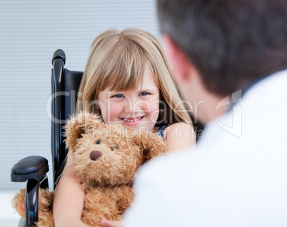 Smiling little girl sitting on the wheelchair with her teddy bea