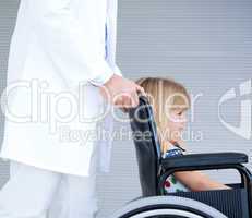 Smiling little girl sitting on the wheelchair supported by a doc