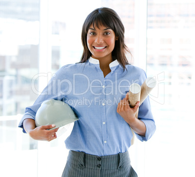 Smiling female architect holding a hardhat and blueprints standi