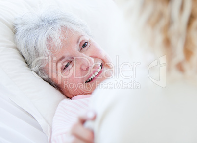 Cheerful senior woman lying on a hospital bed talking with her g