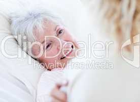 Cheerful senior woman lying on a hospital bed talking with her g