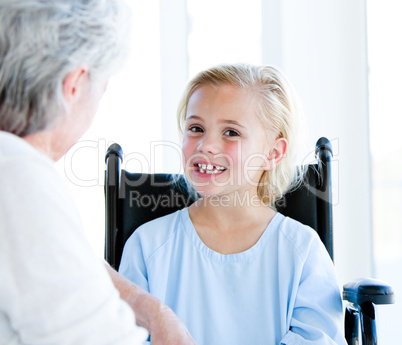 Blond little girl sitting on a wheelchair talking with her grand
