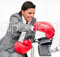 Young businesswoman wearing boxing gloves punching a computer