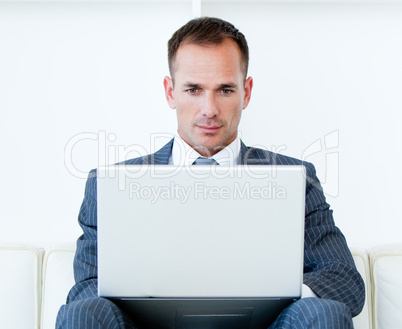 Concentrated businessman using a laptop sitting on a sofa