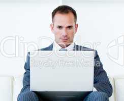 Concentrated businessman using a laptop sitting on a sofa