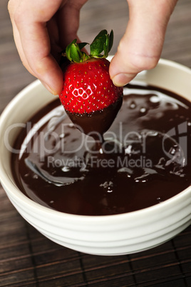 Hand dipping strawberry in chocolate