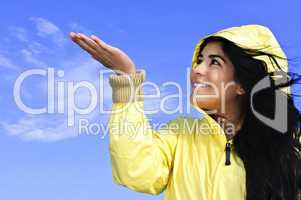 Beautiful young woman in raincoat checking for rain