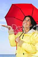 Beautiful young woman in raincoat with umbrella checking for rain