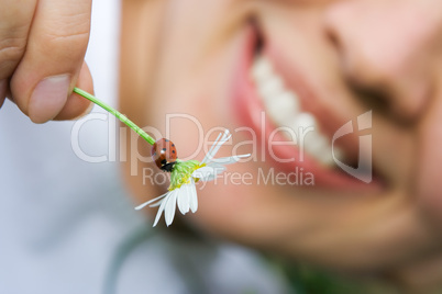 close-up smiling woman holding flower camomile with ladybug