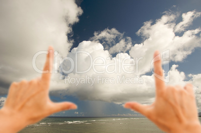 Hands Framing Dramatic Clouds over Tropical Shoreline