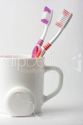 Two toothbrushes in a cup and dental floss