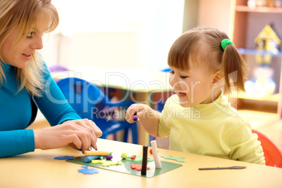 Teacher and little girl play with plasticine