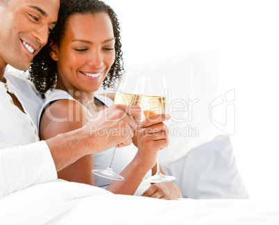 Affectionate couple toasting with Champagne lying on their bed