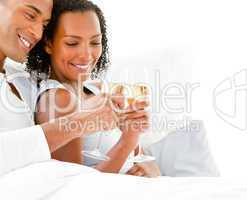 Affectionate couple toasting with Champagne lying on their bed