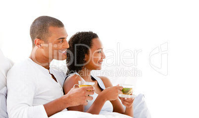 Cheerful couple drinking a cup of tea lying on their bed