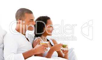 Cheerful couple drinking a cup of tea lying on their bed