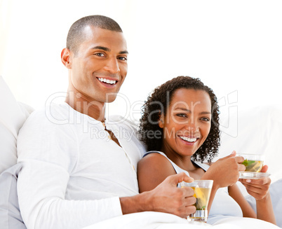 Happy couple drinking a cup of tea lying on their bed