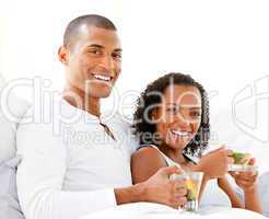 Happy couple drinking a cup of tea lying on their bed