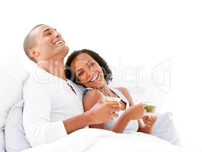 Joyful couple drinking a cup of tea lying on their bed