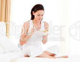 Brunette woman having breakfast sitting on her bed
