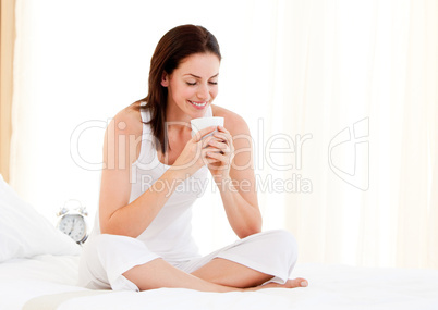 Smiling woman drinking a coffee sitting on her bed