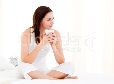 Attractive woman drinking a coffee sitting on her bed
