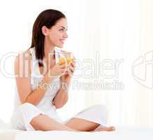 Cheerful woman drinking an orange juice sitting on her bed