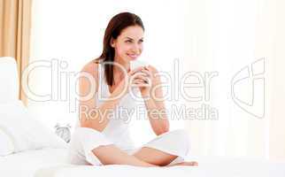 Beautiful woman drinking a coffee sitting on her bed