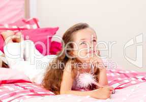 Smiling little girl writing on a notebook lying on her bed