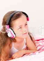 Smiling little girl listening music lying on her bed