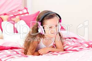Cheerful little girl listening music lying on her bed