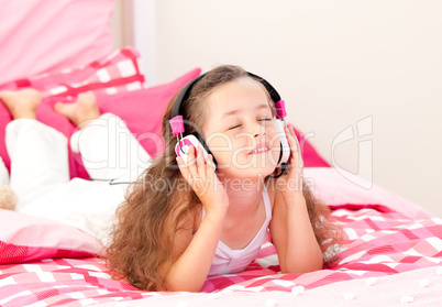 Beautiful little girl listening music lying on her bed