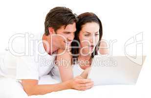 Surprised couple using a computer lying on their bed