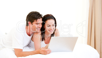 Cheerful couple using a computer lying on their bed