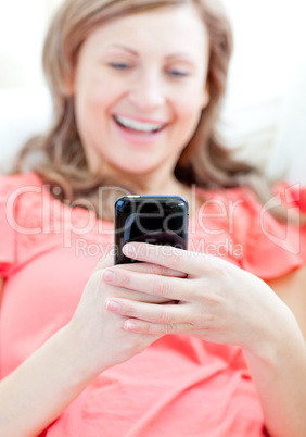 Laughing woman sending a text lying on a sofa