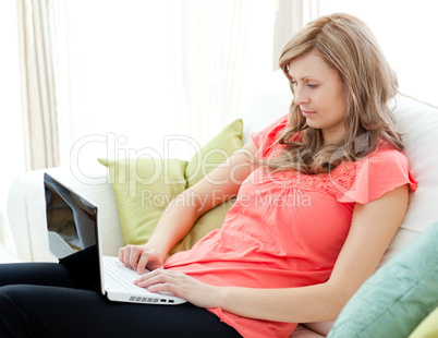 Concentrated woman using a laptop sitting on a sofa