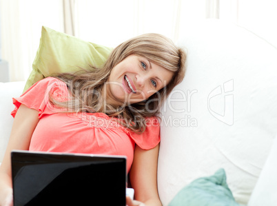 Jolly woman using a laptop sitting on a sofa