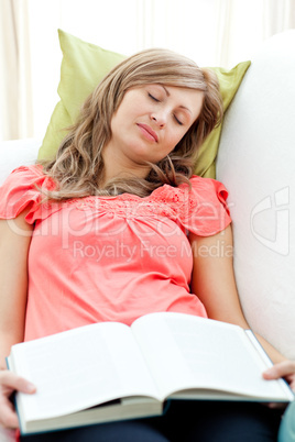 Tired woman reading a book lying on a sofa in the living-room