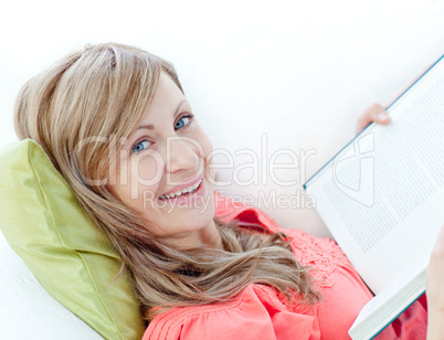 Happy woman reading a book lying on a sofa