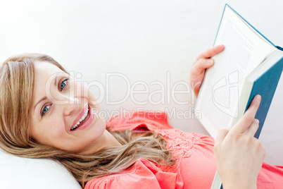 Cheerful woman reading a book lying on a sofa